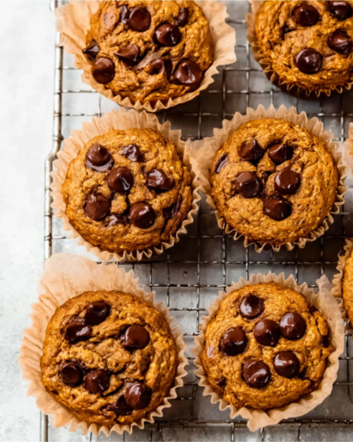 pumpkin-protein-muffins-cooling-rack Pumpkin protein muffins with chocolate chips cooling on a metal rack lined with parchment.