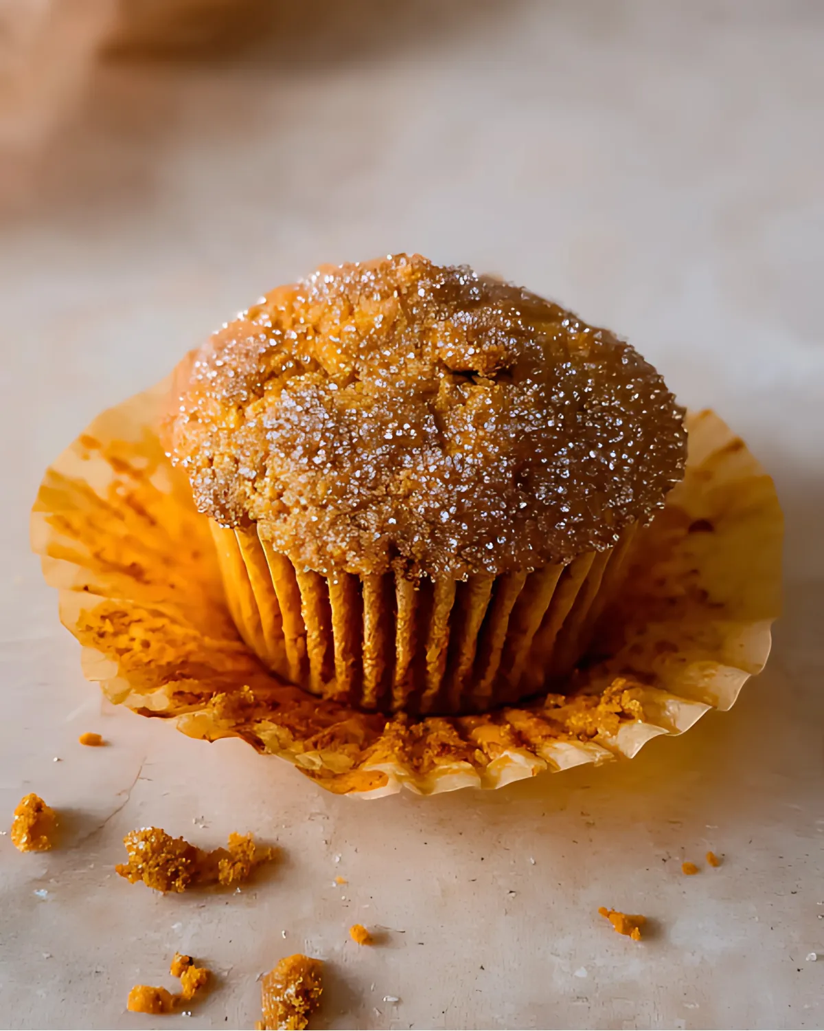 Unwrapped Pumpkin Banana Muffin with sugar topping and crumbs on a light surface
