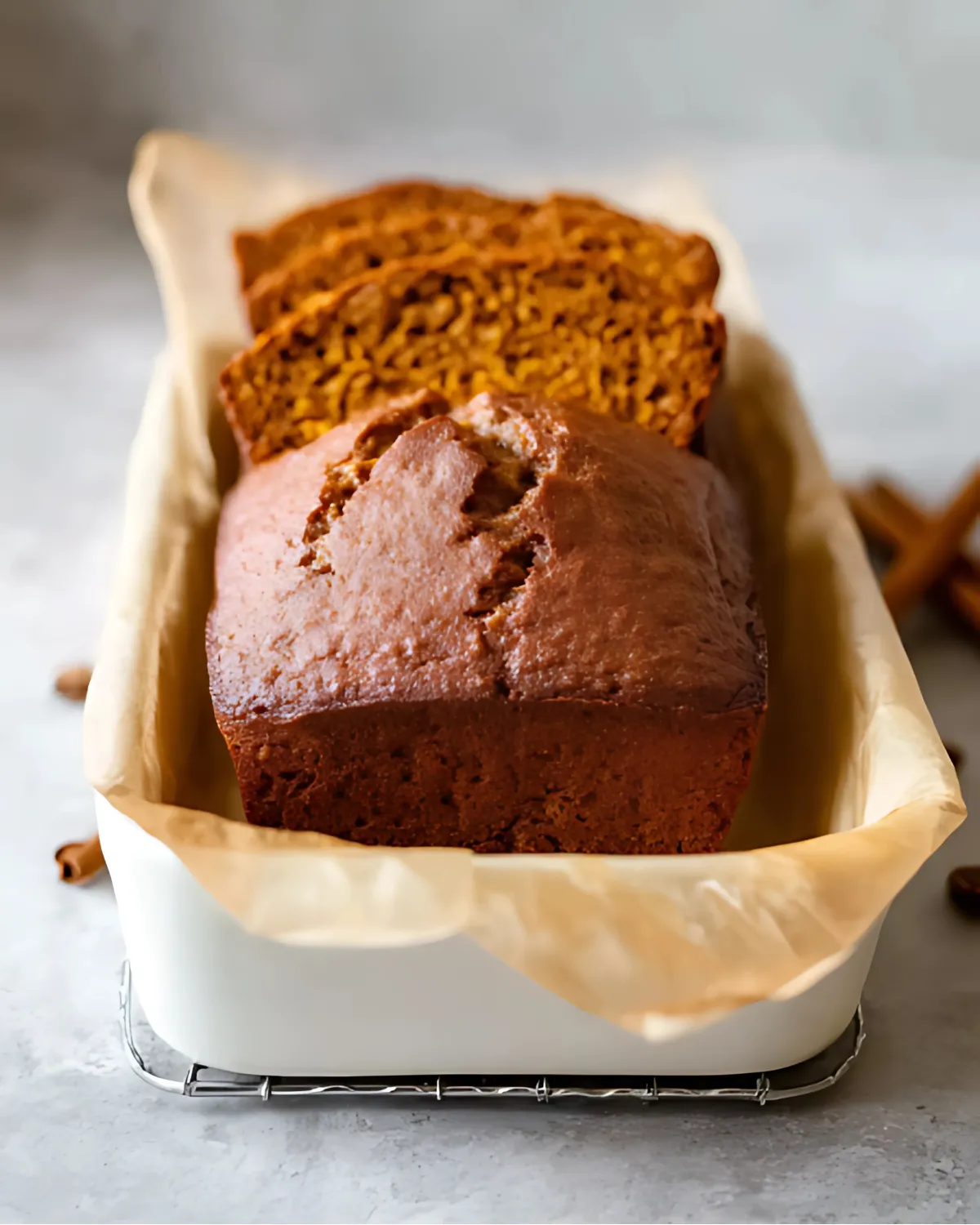 Baked super moist pumpkin bread loaf in a parchment-lined pan, freshly cooled and sliced.