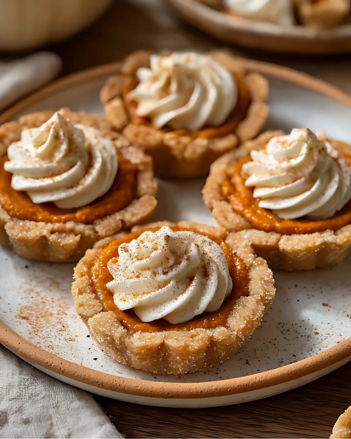 Pumpkin Pie Cookies topped with whipped cream and sprinkled cinnamon on a white plate