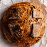 Whole crusty sourdough pumpkin apple bread loaf with golden, caramelized top on parchment paper