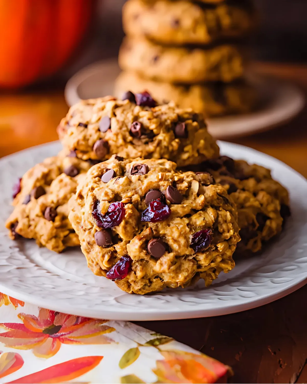 Freshly baked Pumpkin Cranberry Oatmeal Cookies stacked on a white plate with a soft autumn backdrop.