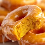 Close-up of a glazed pumpkin donut with a bite taken out, showing moist and fluffy texture