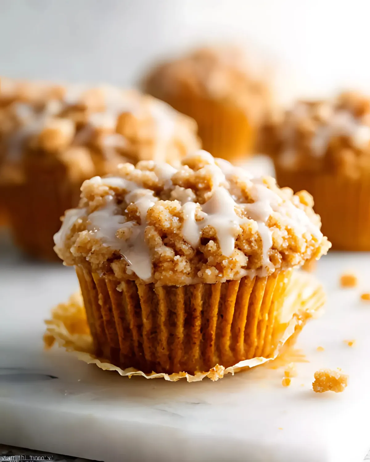pumpkin-crumb-muffins-with-crumb-topping-and-glaze Pumpkin Crumb Muffins with cinnamon crumb topping and vanilla glaze on a marble surface
