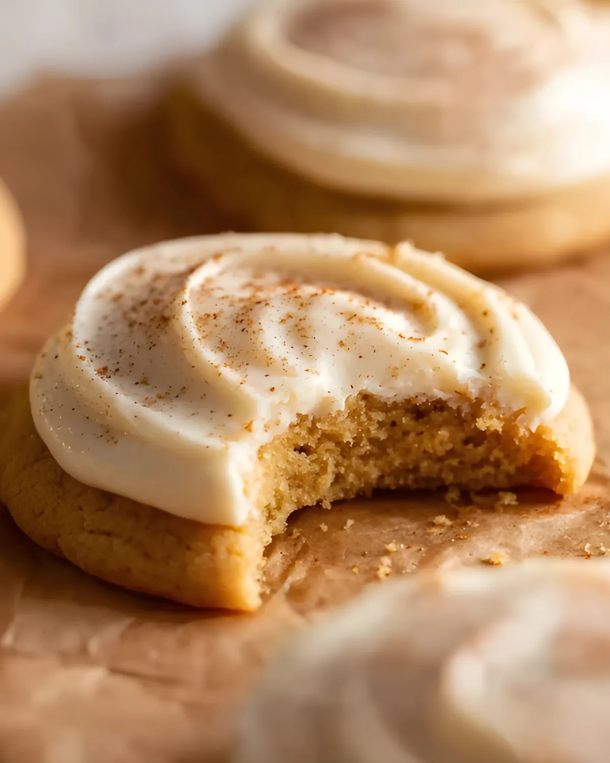 Soft pumpkin sugar cookies with creamy frosting and a sprinkle of cinnamon, one with a bite taken out