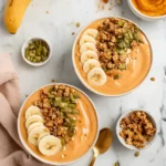 Pumpkin Protein Smoothie Bowl topped with sliced banana, granola, and pumpkin seeds on a marble surface