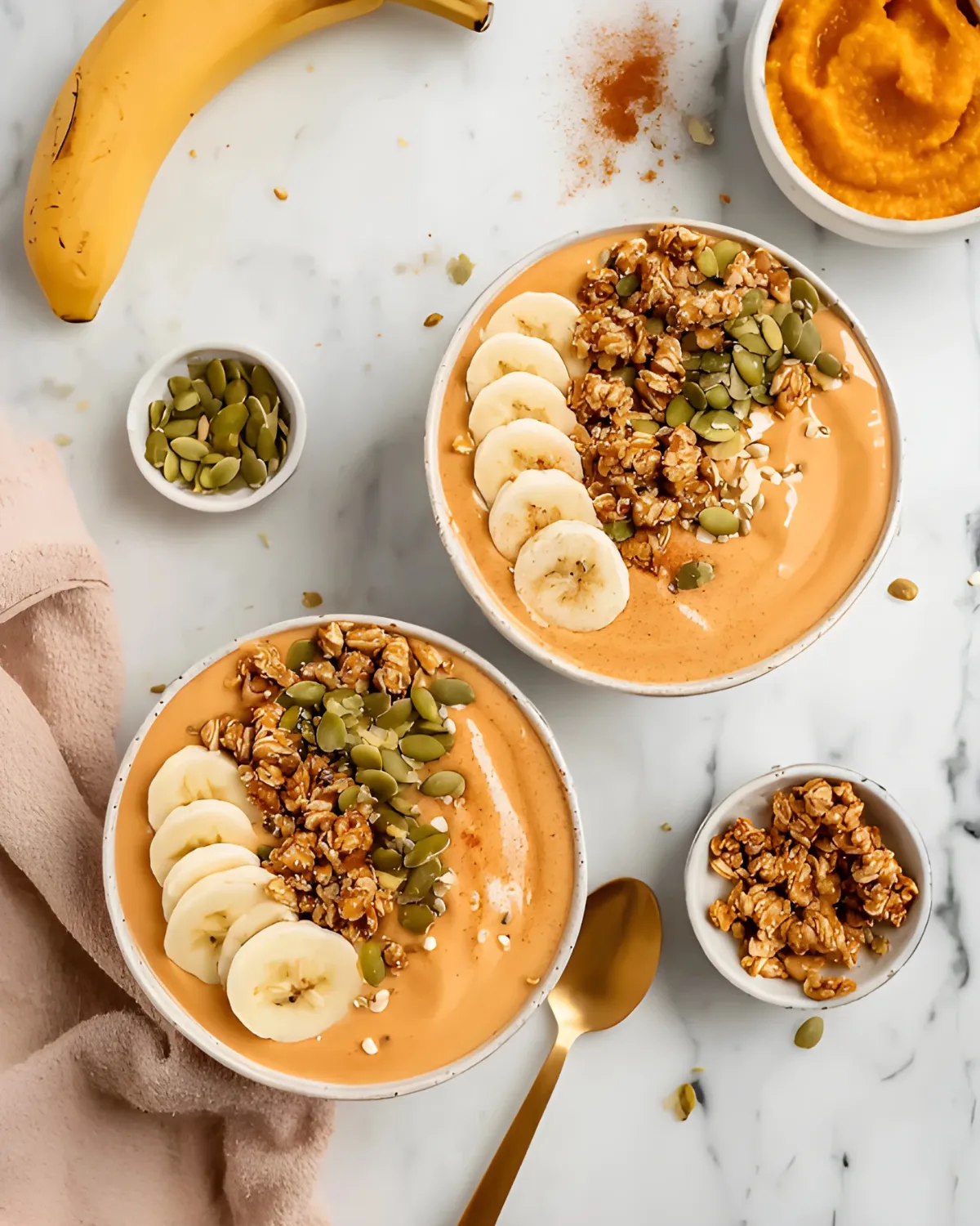 pumpkin-protein-smoothie-bowl-with-banana-and-granola-toppings Pumpkin Protein Smoothie Bowl topped with sliced banana, granola, and pumpkin seeds on a marble surface