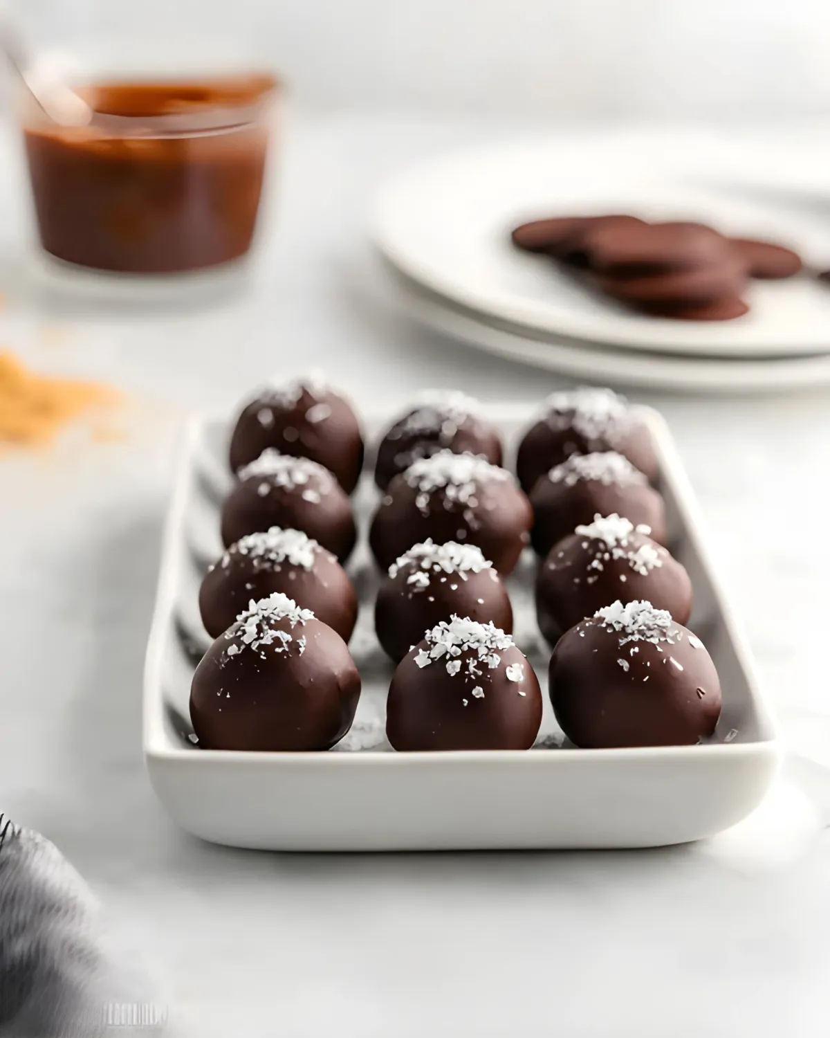 pumpkin-spice-truffles-salted-dark-chocolate-batch Tray of homemade pumpkin spice truffles coated in dark chocolate and topped with flaky sea salt, with baking ingredients in the background.
