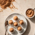 Homemade Keto Pumpkin Fat Bombs arranged on a white plate with crushed nuts and a spoon on the side.