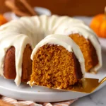 Golden slice of Pumpkin Spice Bundt Cake with creamy glaze being lifted from the cake on a white plate