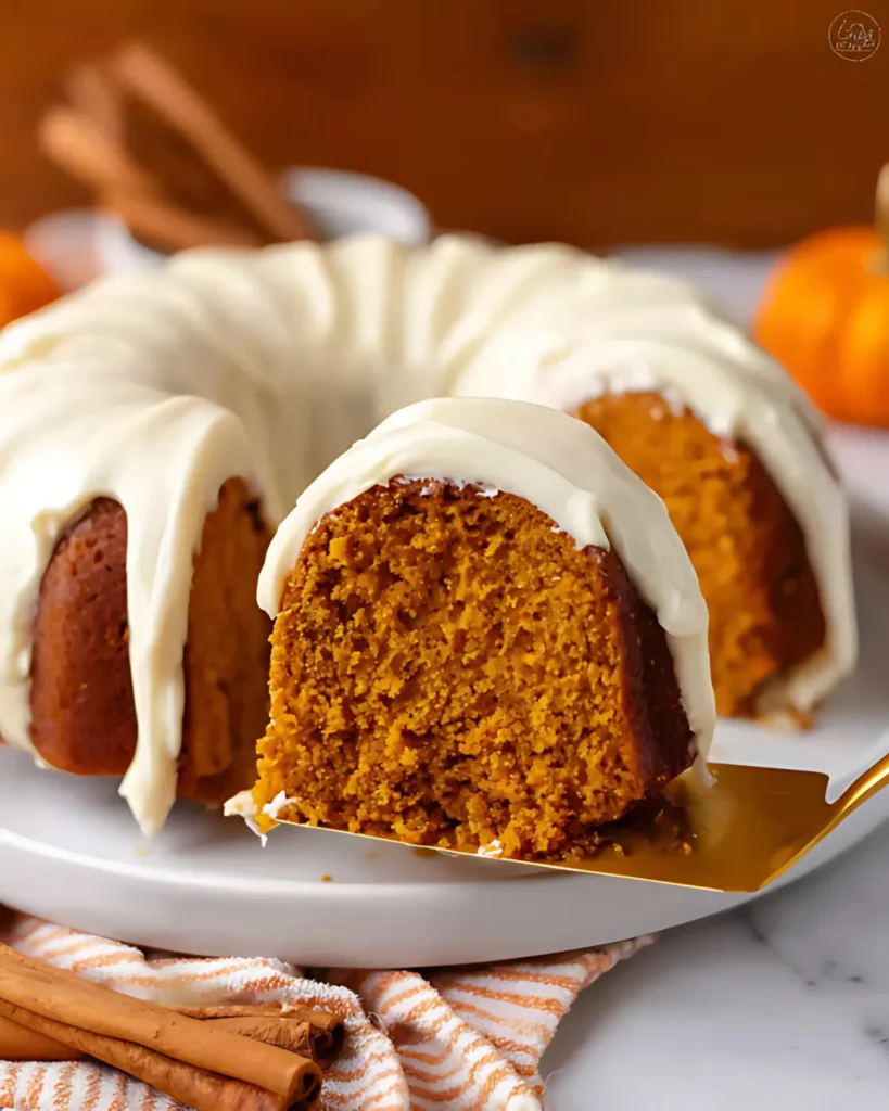Golden slice of Pumpkin Spice Bundt Cake with creamy glaze being lifted from the cake on a white plate