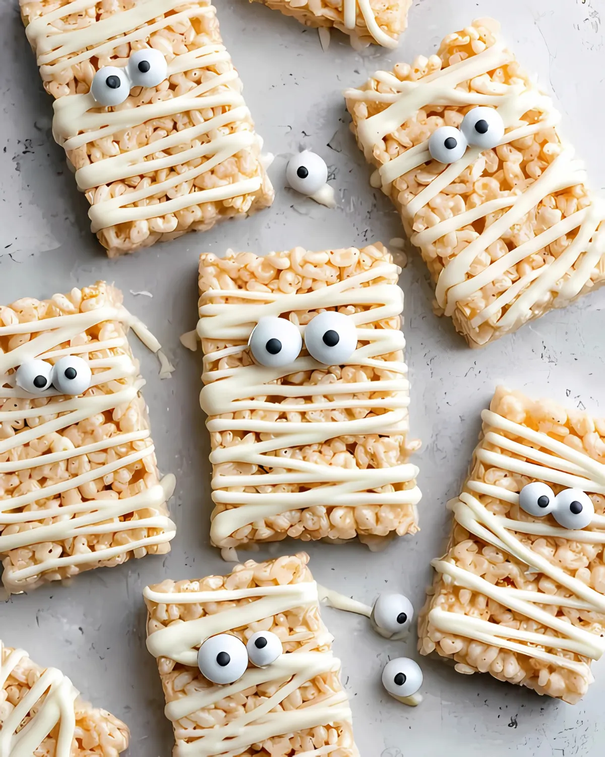 Halloween Rice Krispie Treats decorated like mummies with candy eyes and white chocolate drizzle