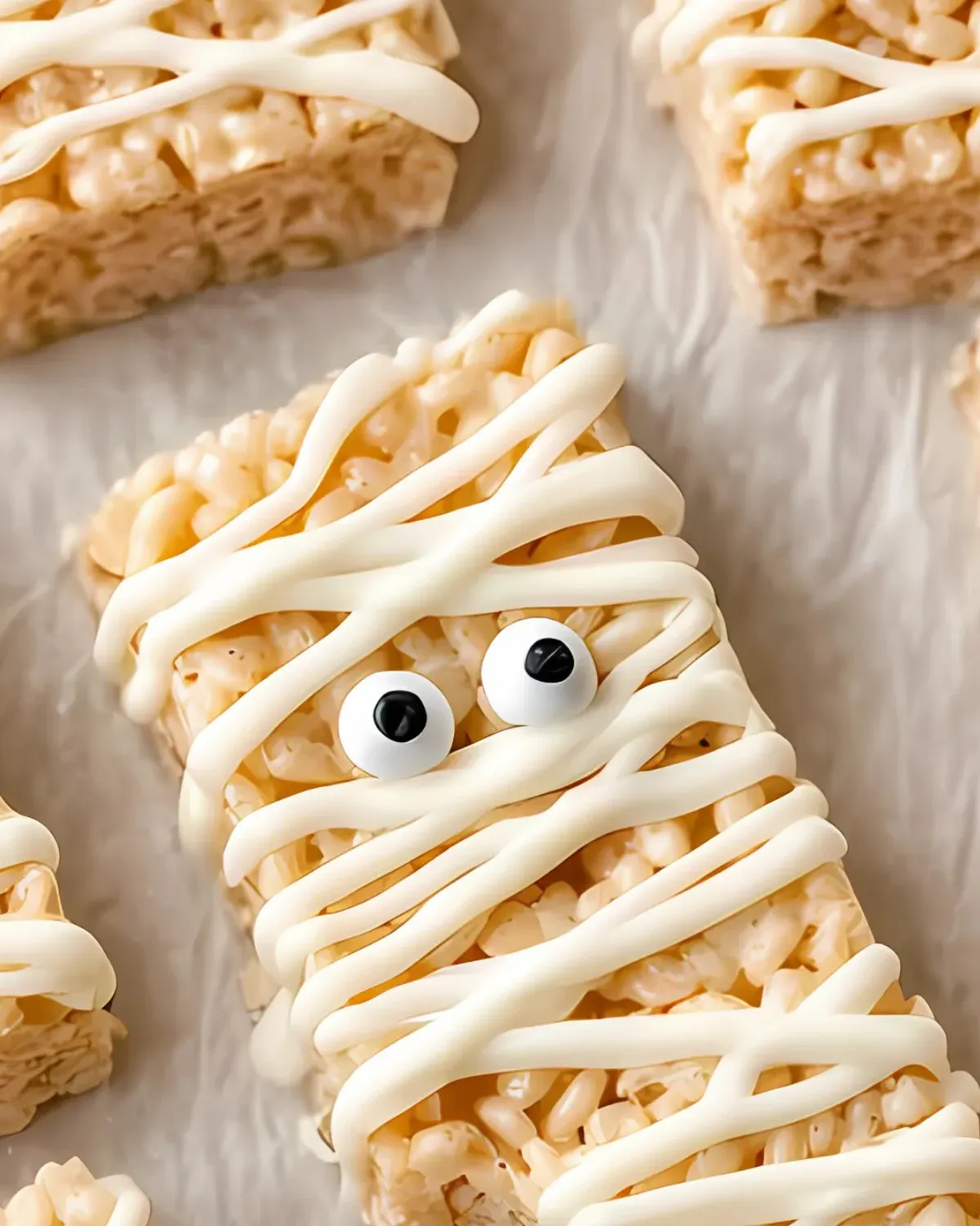 Close-up of Halloween Rice Krispie Treats decorated as mummies with white chocolate drizzle and candy eyes
