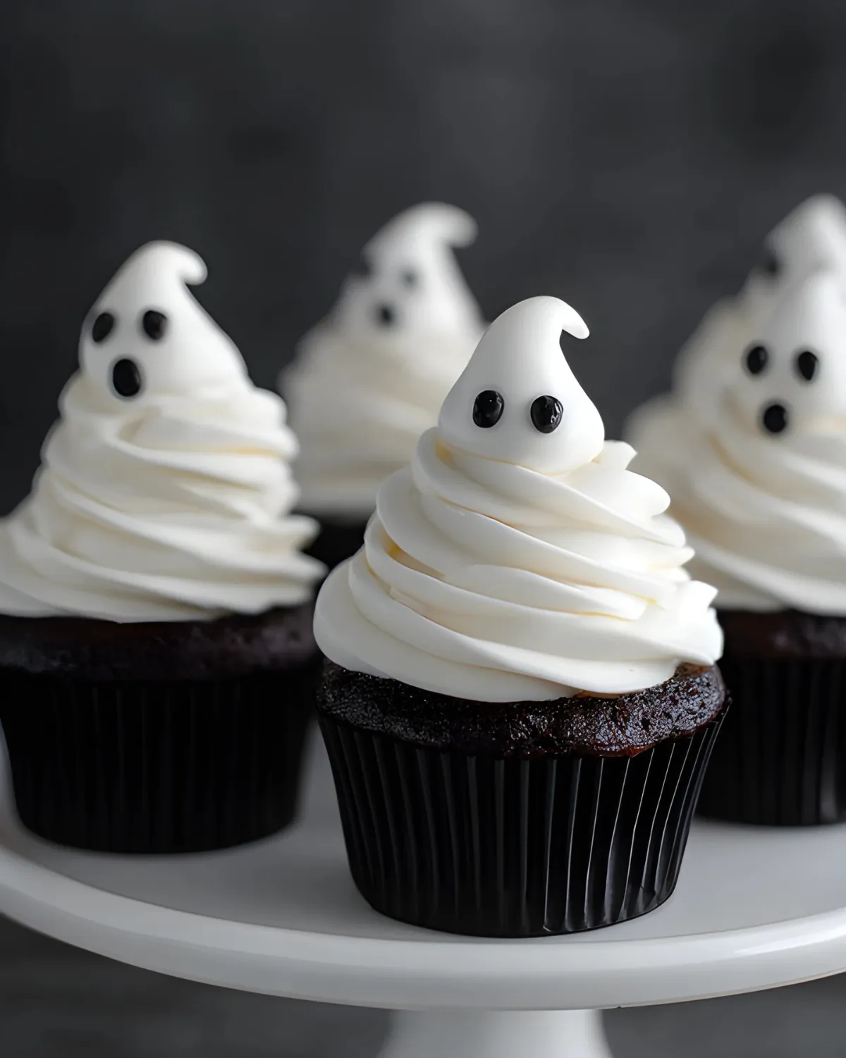Ghost Cupcakes with chocolate base and white ghost-shaped frosting arranged on a cake stand for Halloween