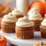 Pumpkin cupcakes topped with cream cheese frosting, surrounded by mini pumpkins and a bottle of milk