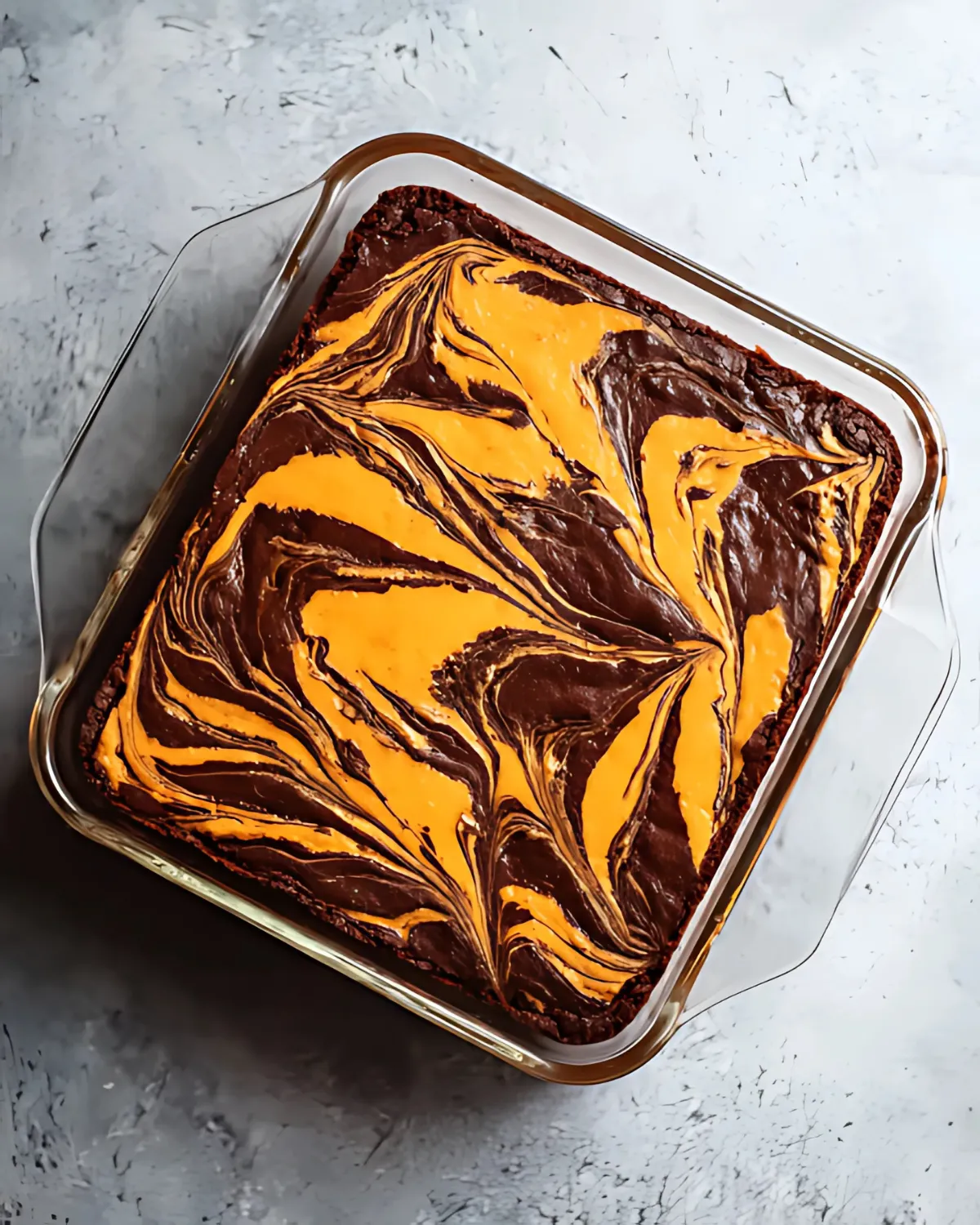 Freshly baked orange cream cheese swirl brownies in a glass dish with a vibrant marbled top.