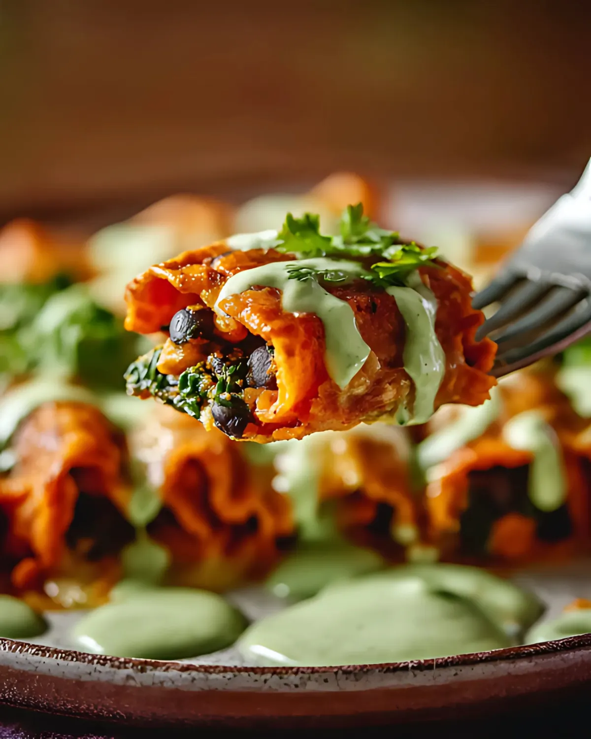 Close-up bite of Pumpkin Black Bean Enchiladas with creamy green sauce and fresh cilantro on a fork