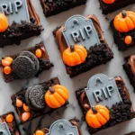 Graveyard brownies cookie tombstones topped with RIP plaques, pumpkins, crushed cookies, and Halloween candies