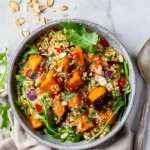Healthy roasted pumpkin quinoa salad with arugula, red onion, bell pepper, and almond flakes in a bowl.