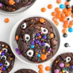 Vegan Halloween cookies decorated with candy eyes, colorful sprinkles, and festive orange, purple, and blue M&Ms