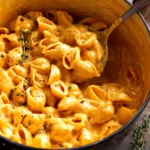 Close-up of stovetop pumpkin mac and cheese in a pot with a ladle and fresh thyme