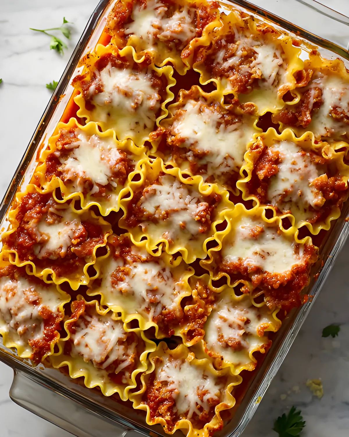 Overhead view of baked Halloween Lasagna Roll-ups in a glass casserole dish, topped with melted cheese and meat sauce