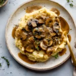Creamy vegan mushroom gravy poured over fluffy mashed potatoes and garnished with fresh herbs.