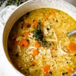 Creamy chicken rice soup with shredded chicken, carrots, and herbs in a rustic white pot