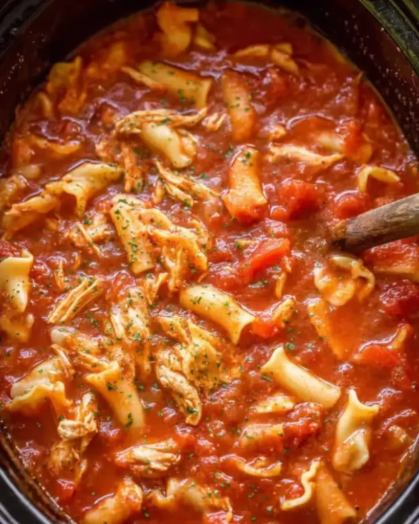 Crockpot chicken parmesan soup simmering in a slow cooker with shredded chicken, pasta, and tomato sauce.