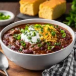 First Place Chili Recipe topped with sour cream, cheddar cheese, and green onions served with cornbread