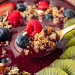 Spoonful of Homemade Acai Smoothie Bowl with granola, berries, and kiwi slices
