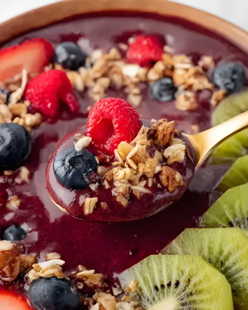 Spoonful of Homemade Acai Smoothie Bowl with granola, berries, and kiwi slices