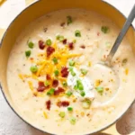 Loaded Potato Soup Recipe served in a yellow Dutch oven, topped with cheddar cheese, bacon bits, green onions, and a dollop of sour cream.