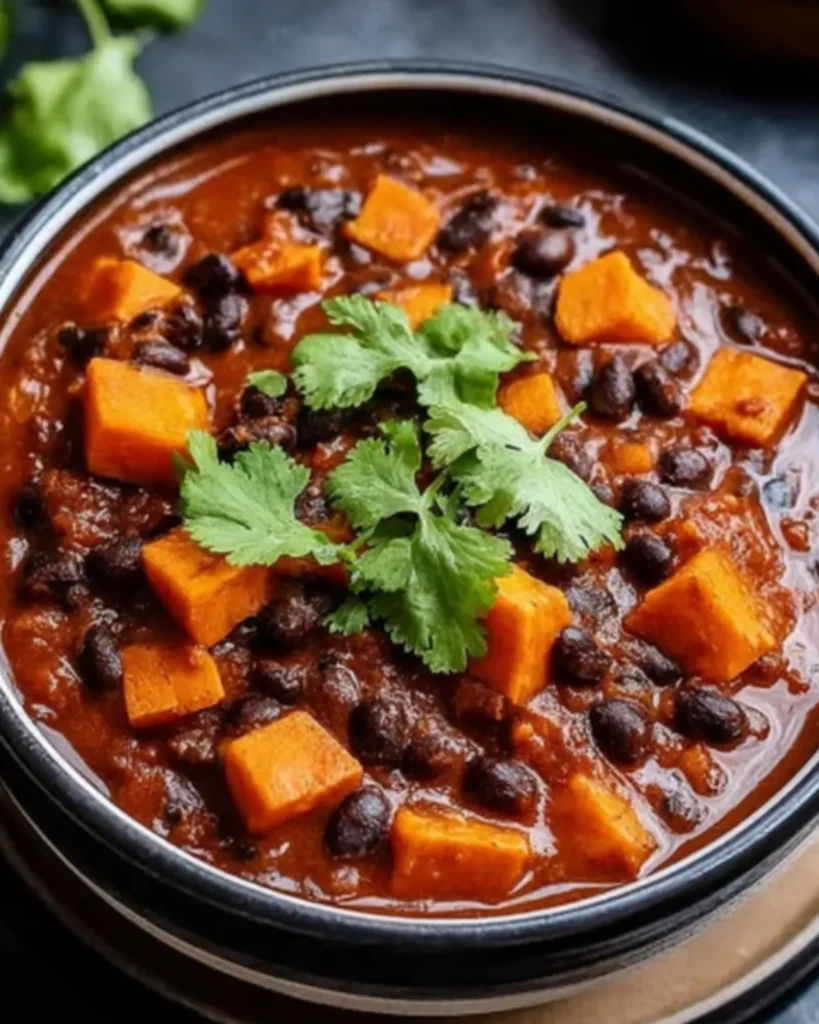 Bowl of sweet potato and black bean chili topped with cilantro on a dark background.