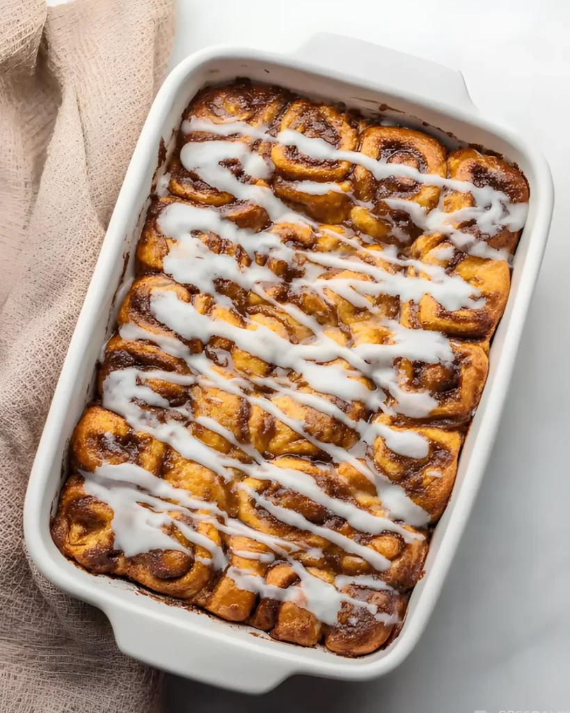 Freshly baked cinnamon roll casserole drizzled with icing in a white baking dish