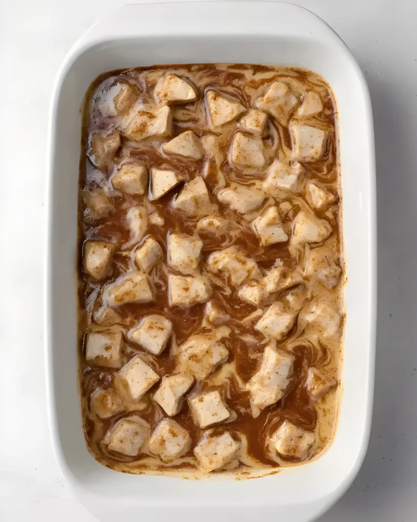 Unbaked cinnamon roll casserole in a white dish with dough pieces and cinnamon filling swirled in custard