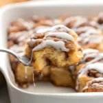 A close-up of cinnamon roll casserole being served with icing dripping off the baked layers