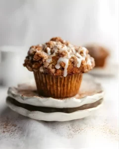 Single coffee cake muffin with a thick cinnamon crumb topping and vanilla glaze on stacked ceramic plates.
