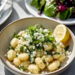 Crispy gnocchi topped with feta cheese, herbs, and a lemon wedge served alongside a fresh salad