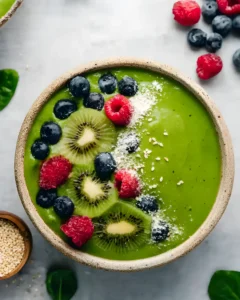 Green smoothie with coconut topped with kiwi slices, blueberries, raspberries, and sprinkled seeds in a rustic bowl