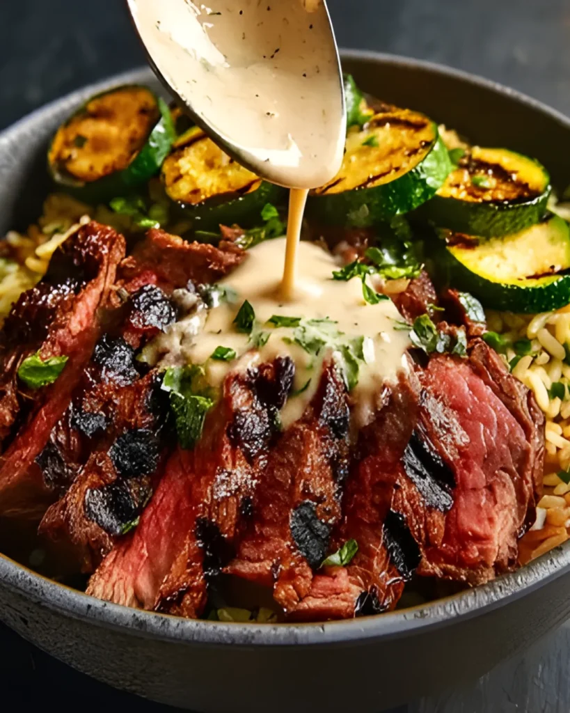 Grilled Steak Bowl with charred steak slices, grilled zucchini, rice, and creamy sauce being spooned on top