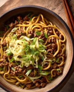 Potsticker Noodle Bowl with ground pork, thick udon noodles, shredded cabbage, and fresh green onions in a rustic wooden bowl.