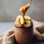 Protein Chocolate Chia Pudding in a jar topped with banana slices and drizzled peanut butter