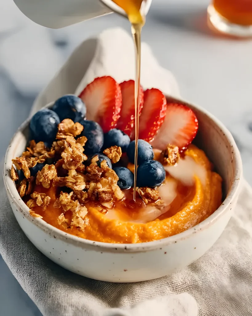 Sweet Potato Breakfast Bowl topped with yogurt, granola, strawberries, and blueberries, drizzled with maple syrup