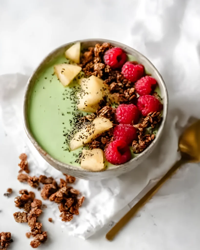 Tropical Matcha with Pineapple breakfast bowl topped with raspberries, pineapple chunks, chia seeds, and granola
