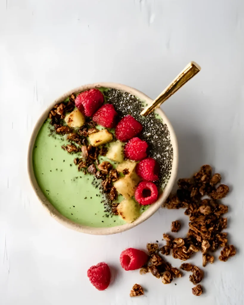 Tropical Matcha with Pineapple smoothie bowl topped with raspberries, granola, banana slices, and chia seeds