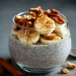 Vanilla chia pudding in a glass topped with sliced bananas, pecans, walnuts, and a sprinkle of cinnamon