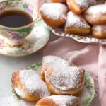 Vanilla French Beignets dusted with powdered sugar served on floral china with a cup of tea