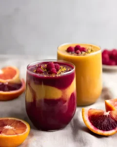 Layered Winter Citrus Smoothie with blood orange and raspberry in glass cups, garnished with fresh berries and citrus slices.