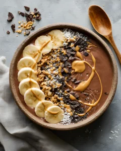 Chocolate Dream Smoothie Bowl topped with banana slices, granola, coconut flakes, dark chocolate chunks, chia seeds, and peanut butter drizzle.